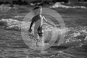 Child running through water close to shore along the sea beach. A boy runs along the sea coast. Rest of children on