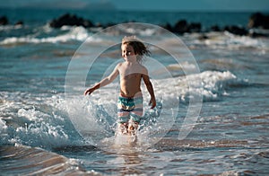 Child running through water close to shore along the sea beach. A boy runs along the sea coast. Rest of children on