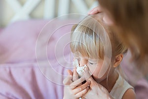 Child with runny nose. Mother helping to blow kid`s nose with paper tissue. Seasonal sickness