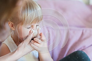 Child with runny nose. Mother helping to blow kid`s nose with paper tissue. Seasonal sickness