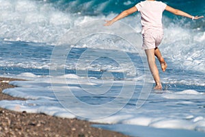 A child runs along the seashore among the waves on a clear day