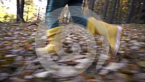 The child runs in yellow rubber boots and jeans on dry autumn leaves, the camera moves chaotically with jerks watching the movemen