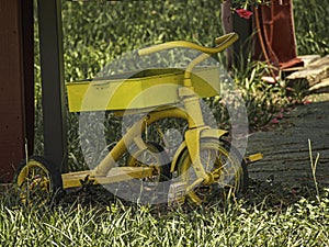 Child\'s antique vintage yellow tricycle parked in the grass.