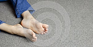 Child`s bare feet. Girl`s legs in jeans. Sitting on the floor.