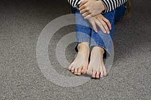 Child`s bare feet. Girl`s legs in jeans. Sitting on the floor.