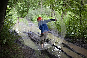 Child`s Boy stands by a large puddle in the park. A child in a construction helmet. Lost son.