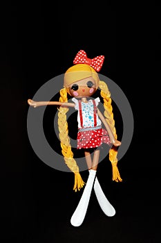 A child`s doll in portrait orientation shown standing against a black wall, black background