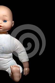 A child`s doll shown sitting, half in/half out of shot on a black background