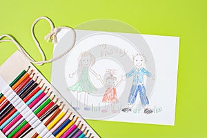 Child`s drawing of a family. Mom, dad and child are drawn with pencils on a sheet of paper on a green background