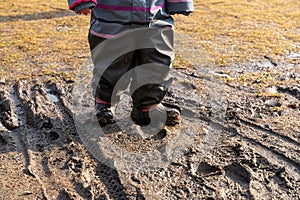 Child`s feet in rubber boots stained in spring mud