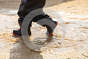 Child`s feet in rubber boots stained in spring mud