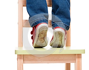 Child's feet standing on the little chair on tiptoes