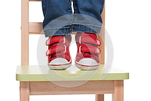 Child's feet standing on the little chair on tiptoes