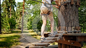 Child's feet walking over wooden rope bridge strung high between trees in forest