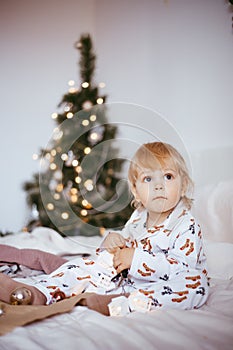 The child`s first Christmas. a pensive little boy is lying in his holiday pyjamas on a bed against the background of a brightly