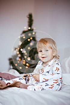 The child`s first Christmas. a pensive little boy is lying in his holiday pyjamas on a bed against the background of a brightly