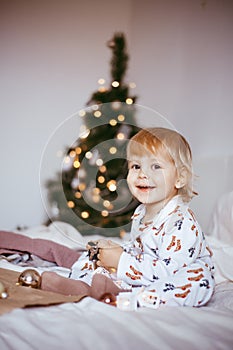 The child`s first Christmas. a pensive little boy is lying in his holiday pyjamas on a bed against the background of a brightly
