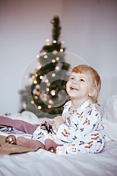 The child`s first Christmas. a pensive little boy is lying in his holiday pyjamas on a bed against the background of a brightly