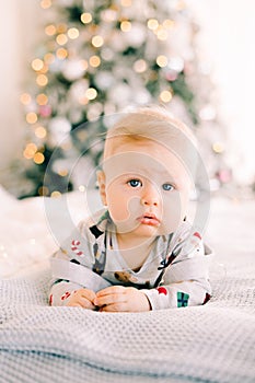 The child`s first Christmas. a pensive sad little boy is lying in a festive costume on the bed against the background of a