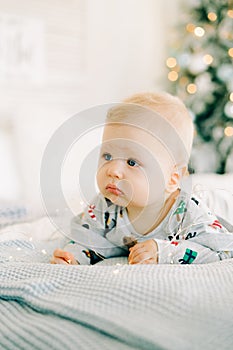 The child`s first Christmas. a pensive sad little boy is lying in a festive costume on the bed against the background of a