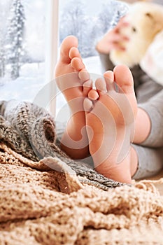 Child`s foots are on a window sill with wool plaid and yarns