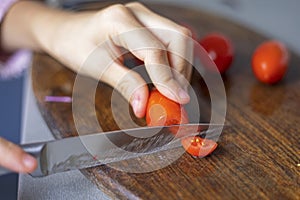 child's hand cuts a cherry tomato into slices on board