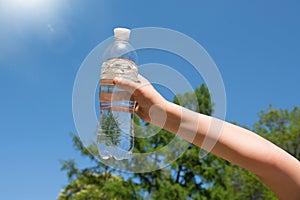 A child& x27;s hand is holding a bottle of drinking water against the blue sky