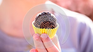 Child`s hand holding Brigadeiro, traditional Brazilian delicacy made with condensed milk, cocoa powder, butter and chocolate photo