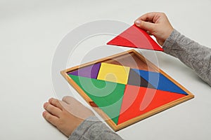 Child`s hand holding a missing piece in a tangram