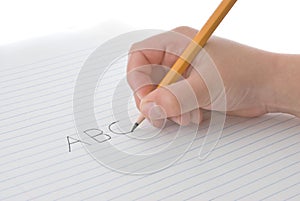 Child's hand holding pencil, writing alphabet on paper