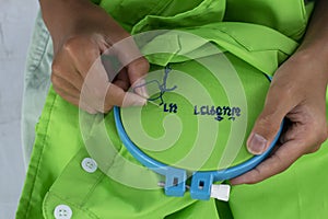 A child`s hand holds a blue plastic embroidery hoop, needle and thread for sewing while embroidering Thai Language.