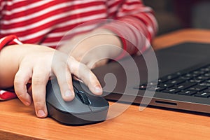 Child`s hand holds a computer mouse, child learns and plays on the computer