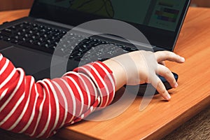 Child`s hand holds a computer mouse, child learns and plays on the computer