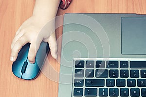 Child`s hand holds a computer mouse, child learns and plays on the computer
