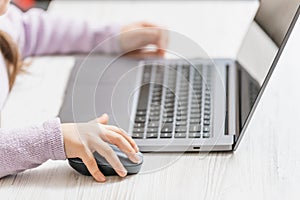 Child`s hand holds a computer mouse, child learns and plays on the computer