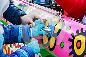 Child`s hand holds doorhandle of pink colorful car