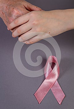 The child's hand holds the hand of the grandmother. Pink ribbon  on grey, top view. Defocus, copy space