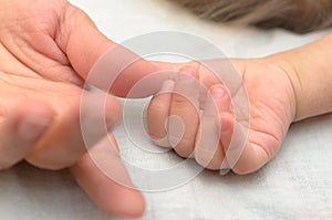 A child`s hand holds Mom by the finger.