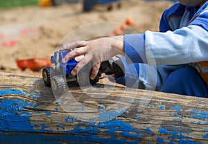 A child`s hand holds a toy car and rolls it on a log. The child plays in the sandbox.