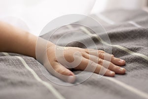 The child`s hand lies on the bed. Gray linens. Bright gentle light.