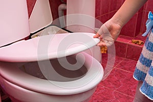 Child`s hand lifts lid of the toilet, close-up