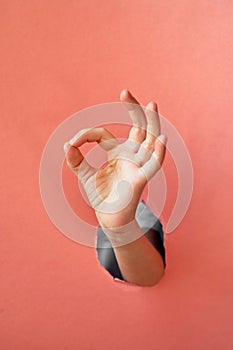 A child`s hand makes a sign, everything will be fine, OK.Trend hand in a hole made of pink paper.