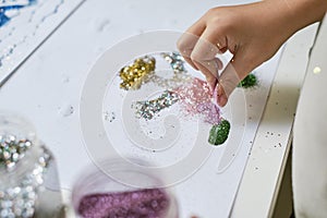 Child`s hand making funny art work with glitter