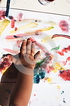 child's hand making his mark on paper painted with tempera