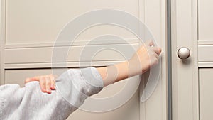 Child's hand opens the closet door. Cute baby girl playing with a wooden cupboard