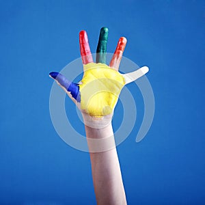 Child's hand painted with multicolored finger paints on blue