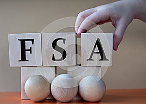 A child's hand places a large cube next to other cubes. FSA acronym concept