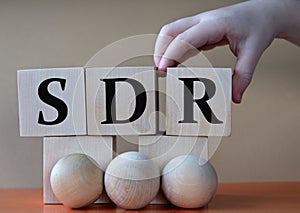 A child's hand places a large cube next to other cubes. SDR acronym concept photo