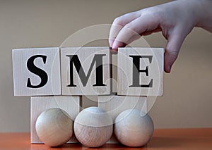 A child's hand places a large cube next to other cubes. SME acronym concept