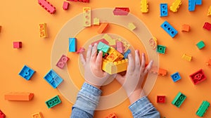 A child\'s hand playing with Lego. There are Legos scattered on the table with a orange background